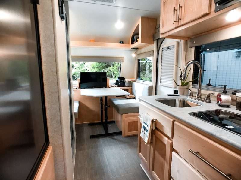 the interior of a small teardrop trailer RV that shows the galley kitchen, convertible dinette, and lots of cabinets for storage