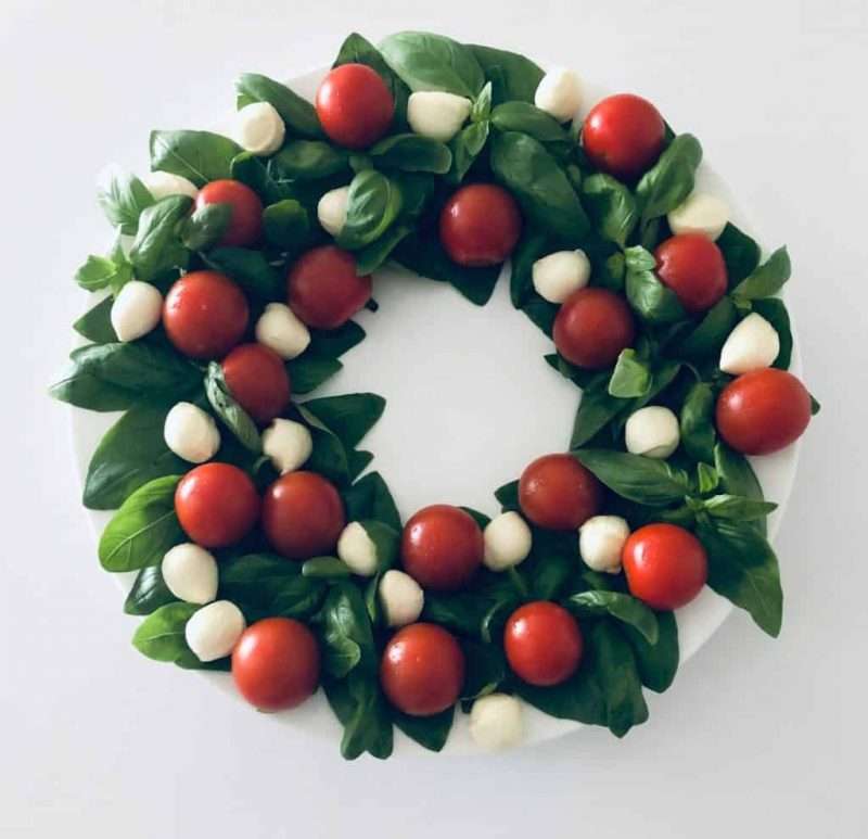 Mozzarella balls and cherry tomatoes are arranged on a bed of greens shaped as a festive wreath for an easy holiday salad recipe.  