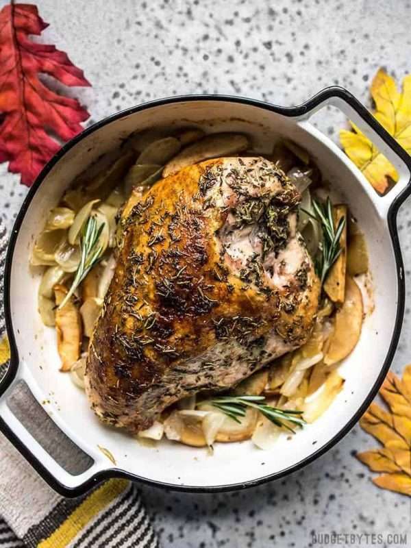A large pot is filled with Cider Roasted Turkey Breast. The pot sits on a speckled countertop with colorful red, yellow, and orange leaves surrounding it.