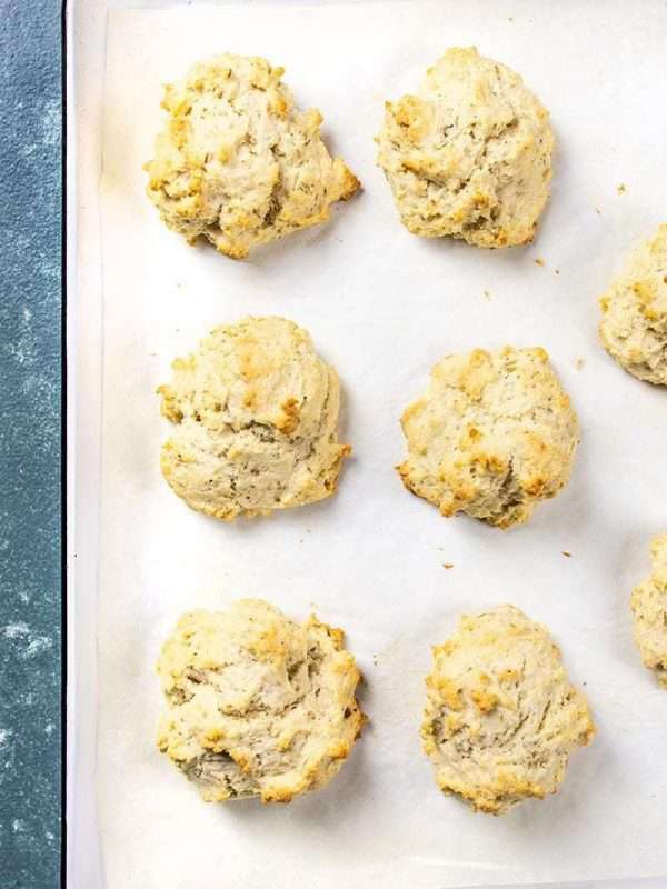 Eight drop biscuits are arranged on a parchment paper-lined baking tray.