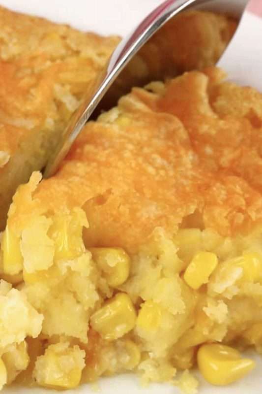 A spoon pierces the crispy cheesy crust of the corn casserole.