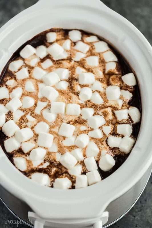 A white crock-pot is filled with homemade hot chocolate and mini marshmallows. 