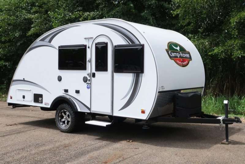 A white Camp Rover teardrop trailer is parked on a concrete pad on a campground.