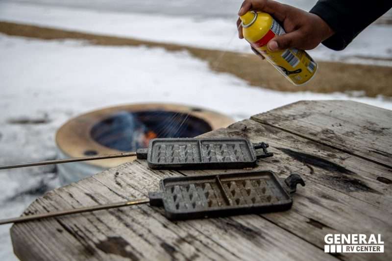 A man sprays non-stick spray onto an open pie iron.