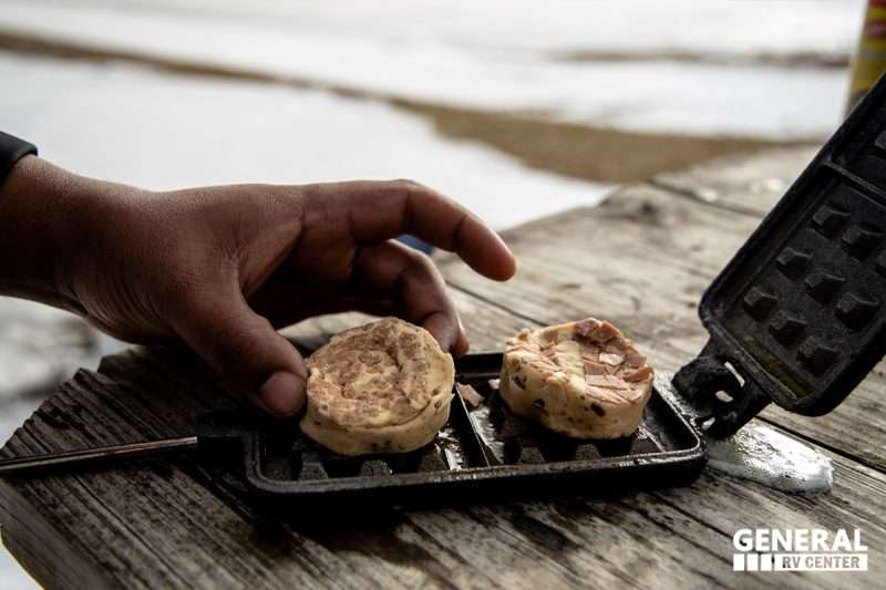 Two cinnamon rolls are placed inside a pie iron to cook.