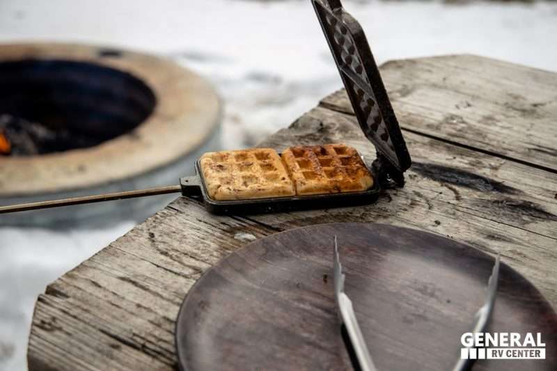 Cooked cinnamon rolls sit inside an open pie iron sitting on a wooden picnic table.