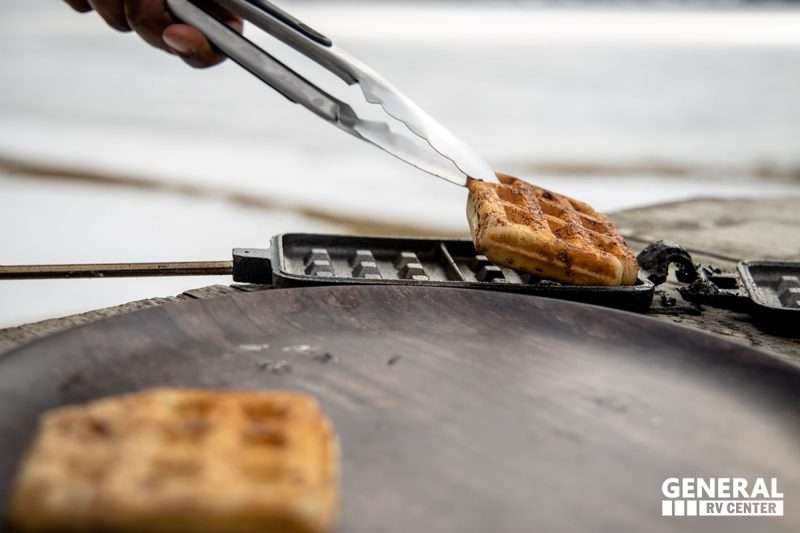 A man uses metal tongs to remove cinnamon rolls from a hot iron.