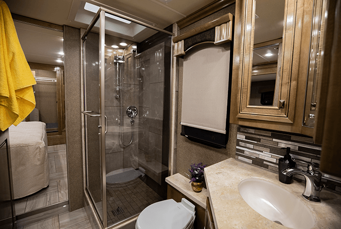 The RV bathroom of the Discovery LXE 40G is spa-like. The large shower is enclosed with glass walls. Chrome fixtures and glossy wood cabinets add a premium feel. The toilet is adjacent to the corner vanity, above which is a mirrored medicine cabinet.