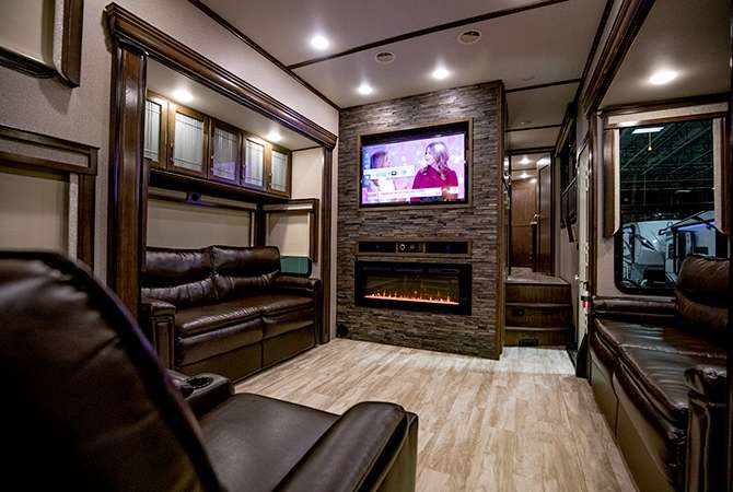 A photo of the RV living area of the Grand Design Solitude 390RK is designed an entertainment center with builtin fireplace. The two couches are opposite each other, with adjacent theater seating.