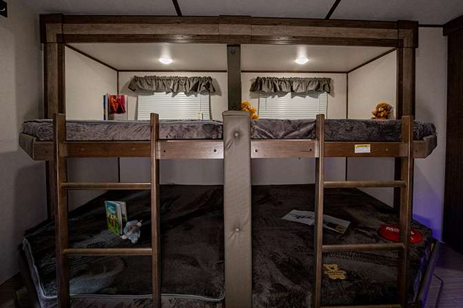 A photo of the side by side bunk beds in the quad bunkroom of the Keystone Passport 3400QD. Each top bunk is accessible via a built in ladder. Various toys are strew across the mattresses.