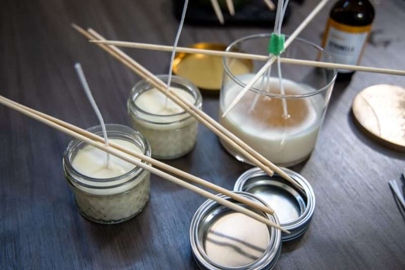 Two small glass containers and one larger glass votive with candle wax are left to cool on a table. The wicks of the candles are held upright by bamboo skewers. 