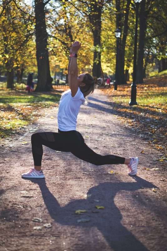 A woman practices yoga in a park. It is a sunny fall day and there are lots of fallen leaves from the changing trees around her and in the background.