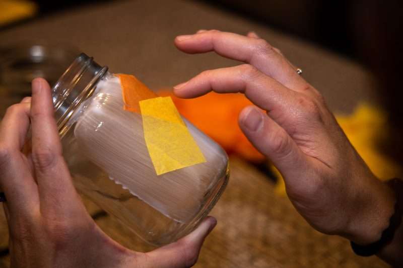 A woman applies tissue paper squares to the glue covered mason jar.