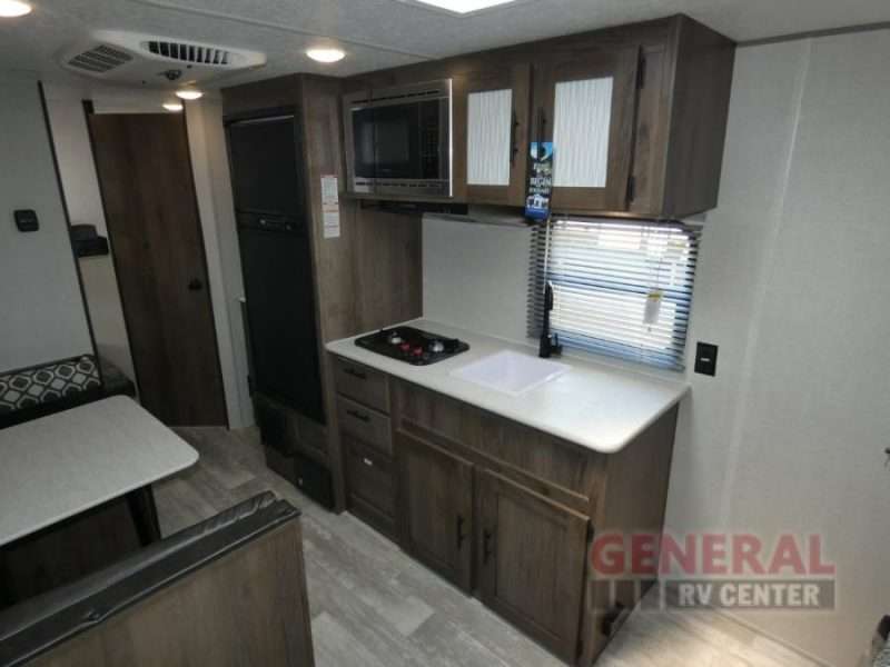 The galley kitchen of the Avenger LT 22BH has a two burner cooktop, sink, microwave and refrigerator with freezer. Across from the kitchen is the booth dining area.