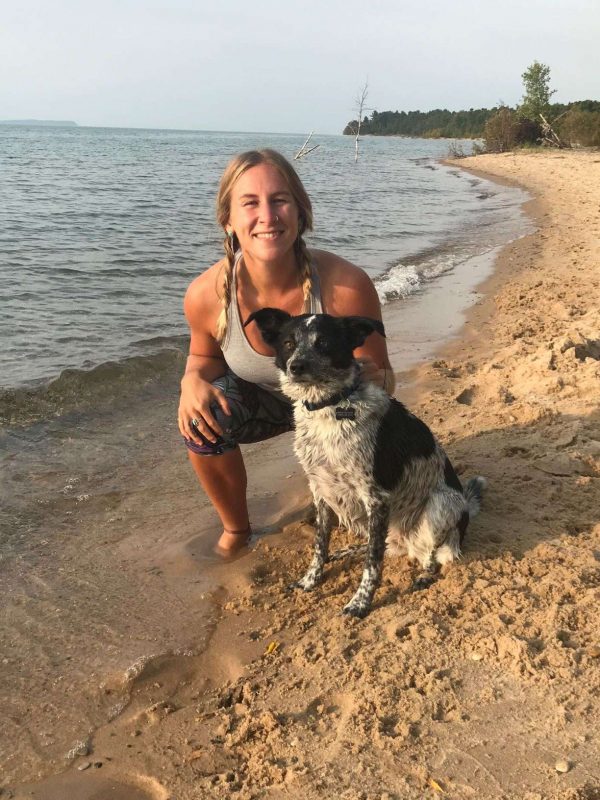 A photo of a young blond woman and her dog on a sandy beach.