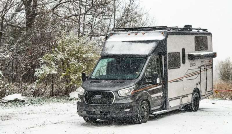 A Winnebago EKKO motorhome is parked outside on a snowy day. The ground and trees in the background are covered with a thin layer of fresh white snow.