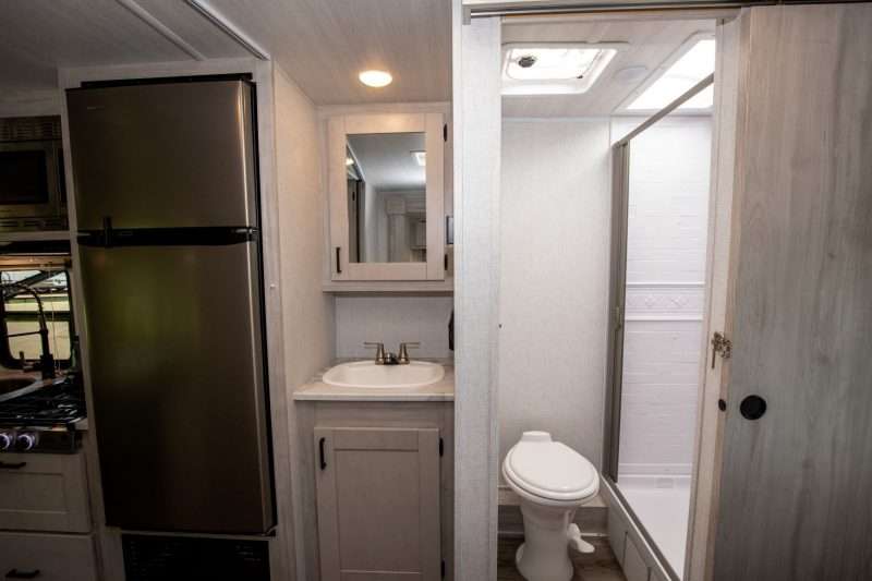 An interior photo of the Entrada 2200S class c motorhome shows the shower and toilet are in the bathroom while the sink and vanity are located just outside the bathroom. The light and bright Granite Peak décor is continued throughout the RV.
