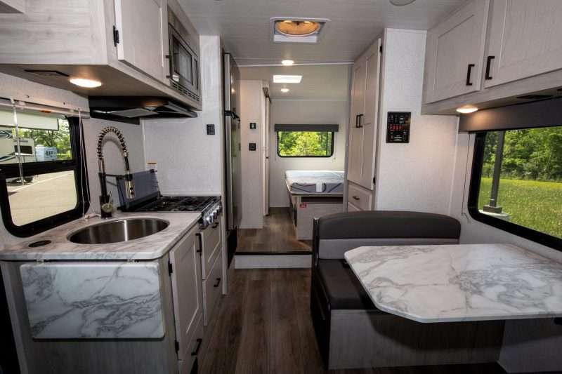 The interior of the Entrada 2200S class c motorhome features a light gray and white color palette. The counters and dinette table are marbled white and gray to compliment the hardwood cabinetry, while the dark gray fabric of the dinette seating provides contrast.