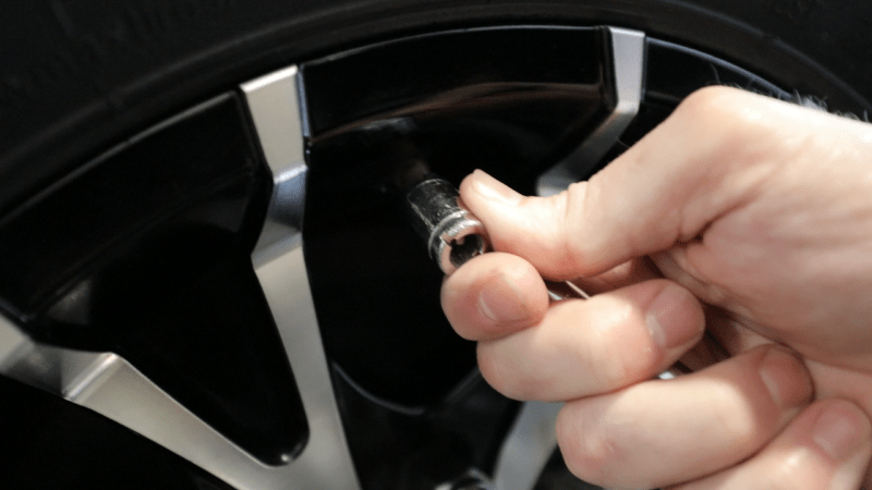 A hand uses a tire pressure gauge to check the pressure in a tire.