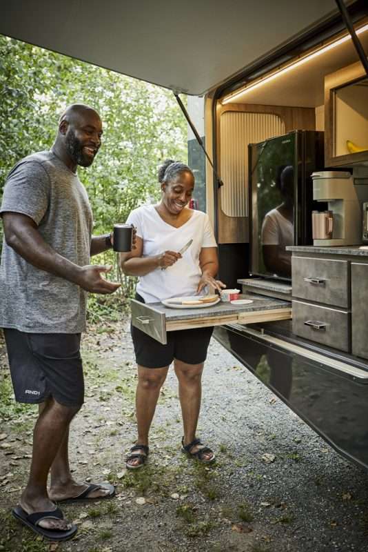 A man and woman making breakfast with their RV's outdoor kitchen.