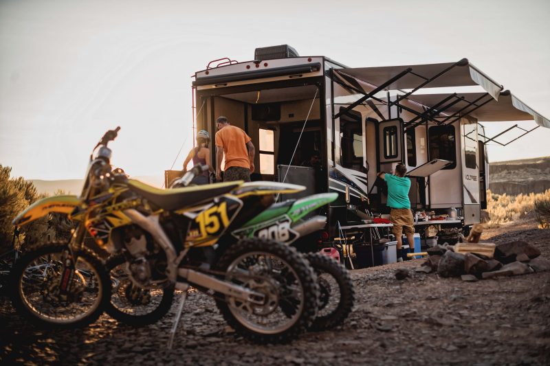 Two dirt bikes sit near a toy hauler RV