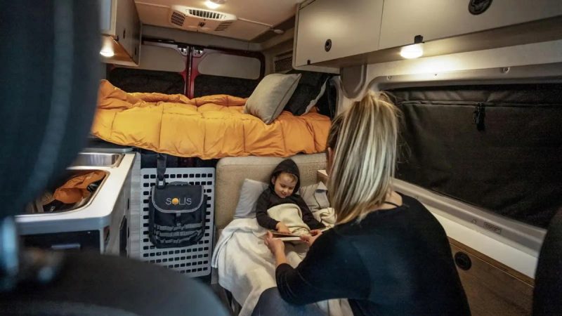 A woman reads to a child tucked into bed inside a Solis Pocket Class B motorhome. 