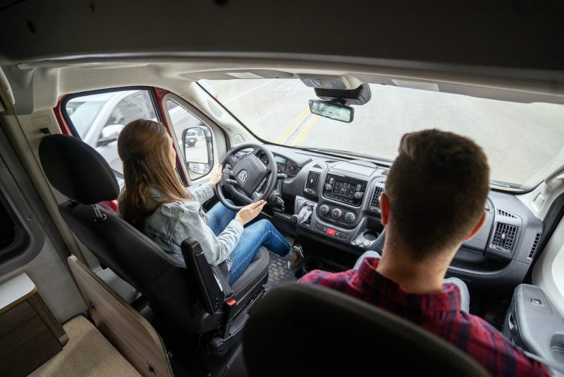 A woman drives a Winnebago Solis Pocket while a male companion rides in the passenger seat.