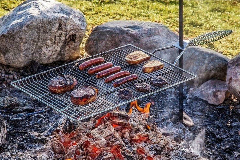 A grill rack filled with food - including burgers and hotdogs - cooks over a campfire. 