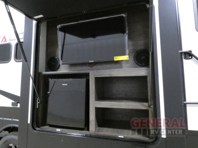 The exterior kitchen of the Alliance RV Valor fifth wheel toy hauler has everything you need to relax outdoors after a great day of riding the trails. An open compartment reveals a flat screen TV and mini fridge on the exterior of the RV.