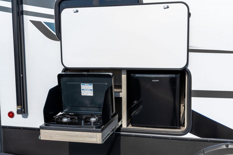 Keystone Passport 219BH SL Series Travel trailer's exterior kitchen includes a mini fridge and two burner cook-top.