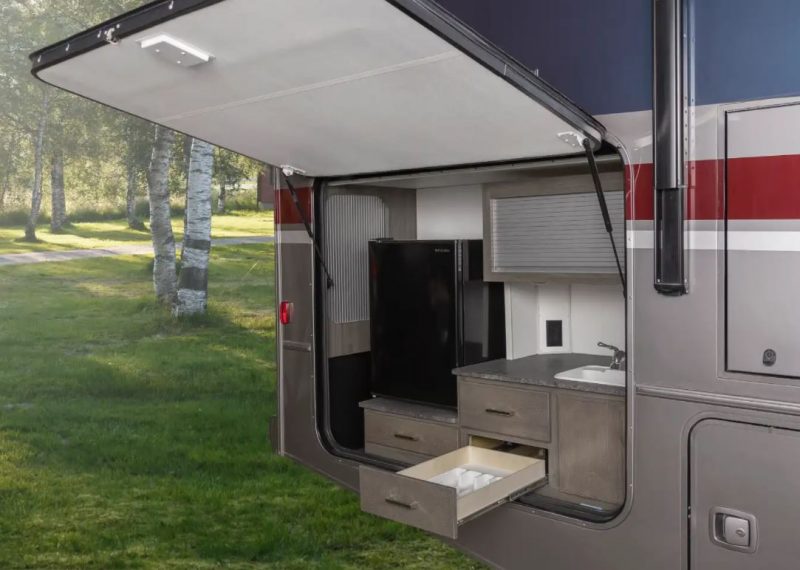 The Winnebago Adventurer Class A motorhome has an outdoor kitchen complete with sink, mini fridge, and counter top space for making meals.
