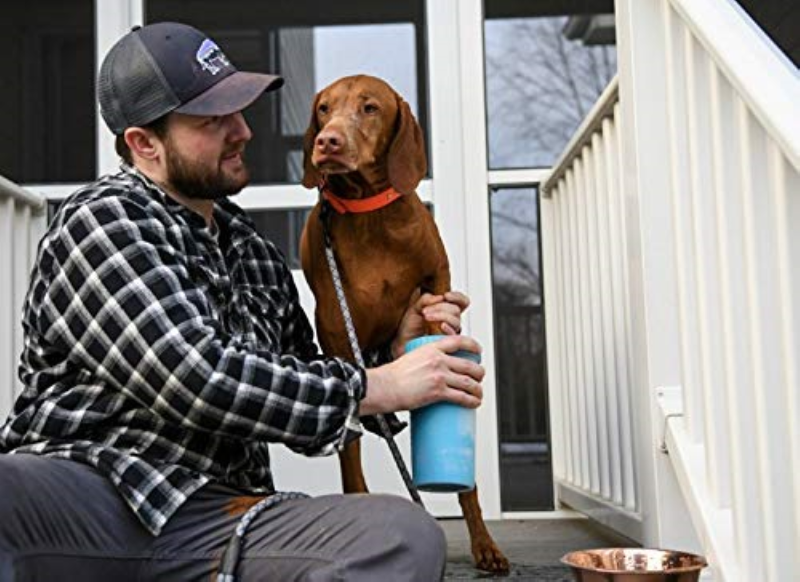 A man sitting on the porch with his brown dog. One of the dog's paws is getting cleaned in the Mud buster Paw Cleaner held by the man.