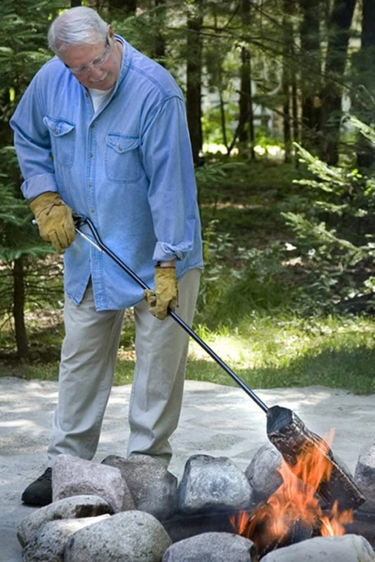 An older gentleman using the Pyroclaw to move wood in a campfire.
