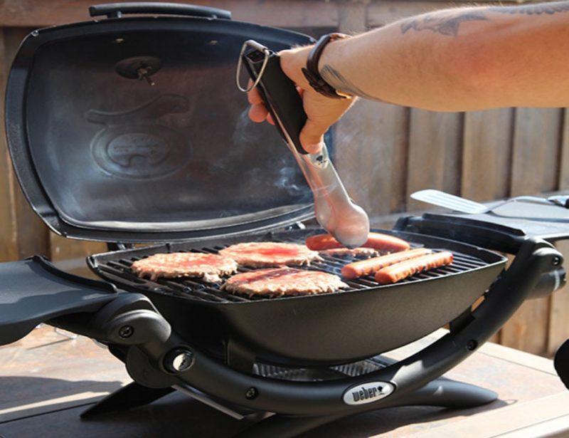 A man is flipping hotdogs on the Weber Q 2200 grill.