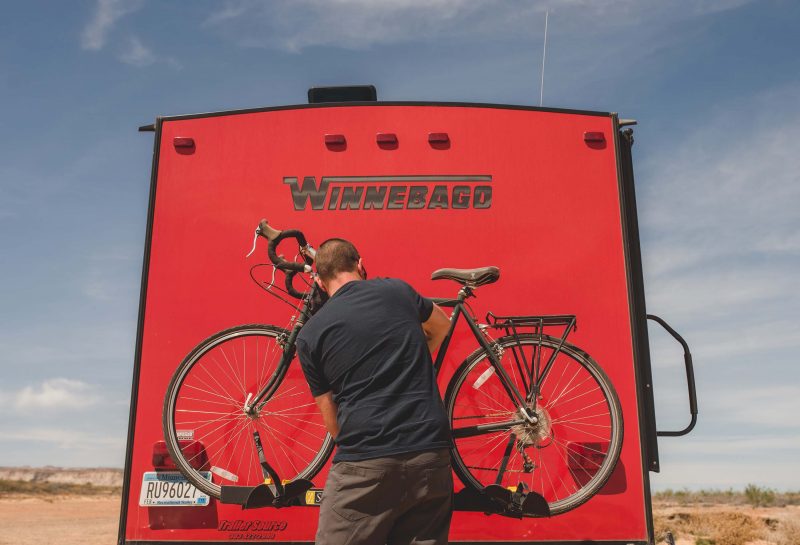 A man unloading a bicycle from the back of his travel trailer.