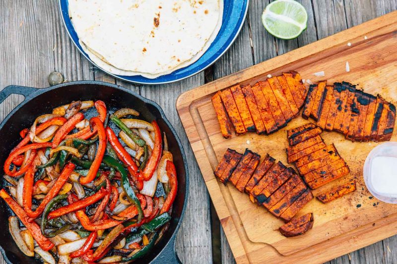 Cooked Grilled Sweet Potatoes, veggies, and tortillas are on a table to be assembled into fajitas.
