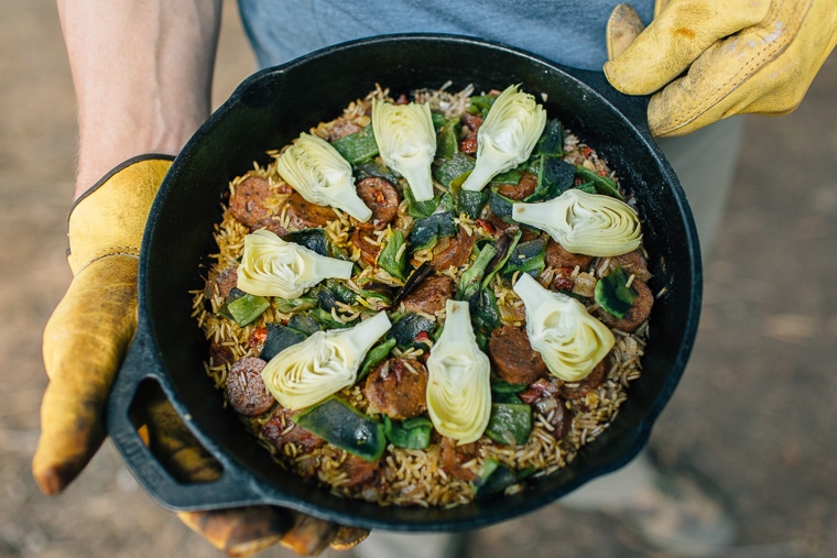 A man holding the freshly made Artichoke and Poblano Campfire Paella.