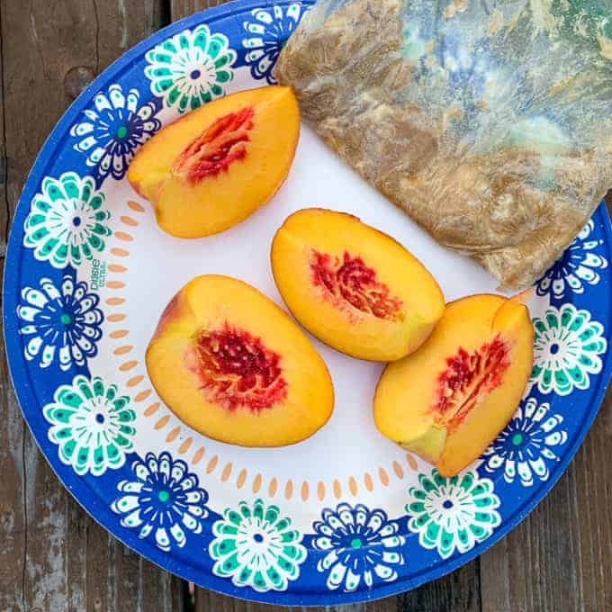 Four sliced peaches are sitting on a plate with a bag of brown sugar and butter mixture.