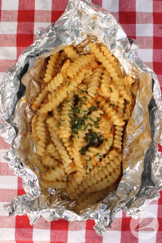 Cooked Cheesy Fries with chives on top still in the Tinfoil packet.