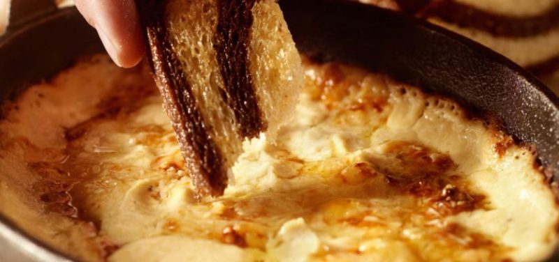 A piece of bread being dipped into the Beer Cheese Dip.