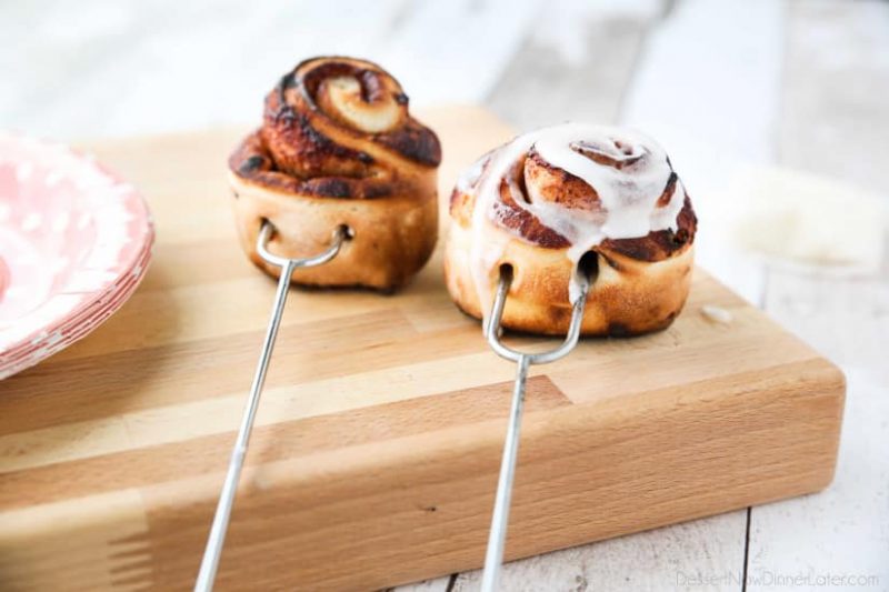 Campfire Cinnamon Rolls sitting on a table with icing on top of one.