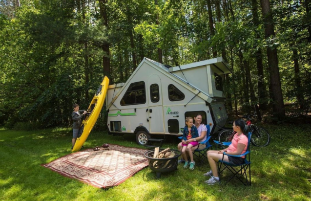 A group of people sit outside a new Aliner Expedition popup camper