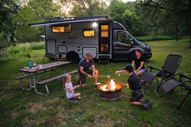 A family of four is sitting around a campfire roasting marshmallows.