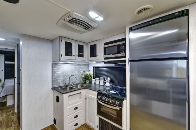 Stainless steel kitchen appliances (fridge, microwave, oven and sink) inside the new Heartland Trail Runner travel trailer