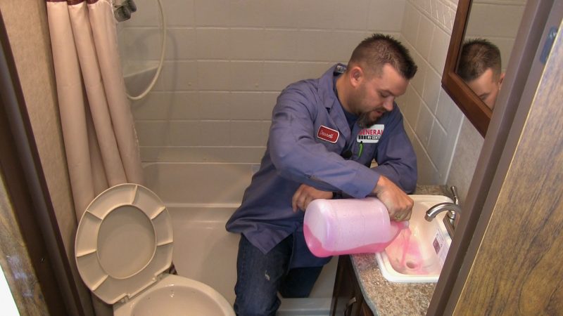A man pours RV anti-freeze in sink drains to winterize the RV's plumbing.