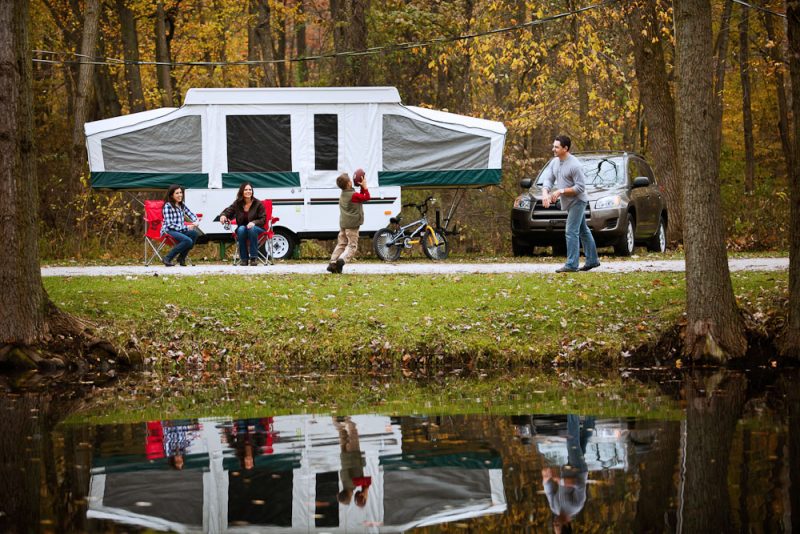 A family enjoying a game of football by their popup camper.