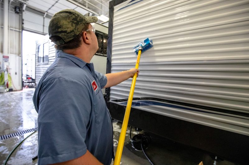 An RV technician cleaning the outside of an RV after dewinterizing it.
