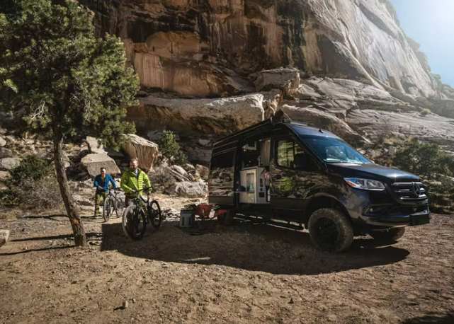 A Thor Sanctuary Class B RV is parked near a large rock formation.