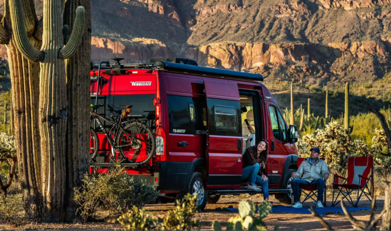 Exterior photo of a Winnebago Travato Class B RV parked in a desert next to tall cacti. 