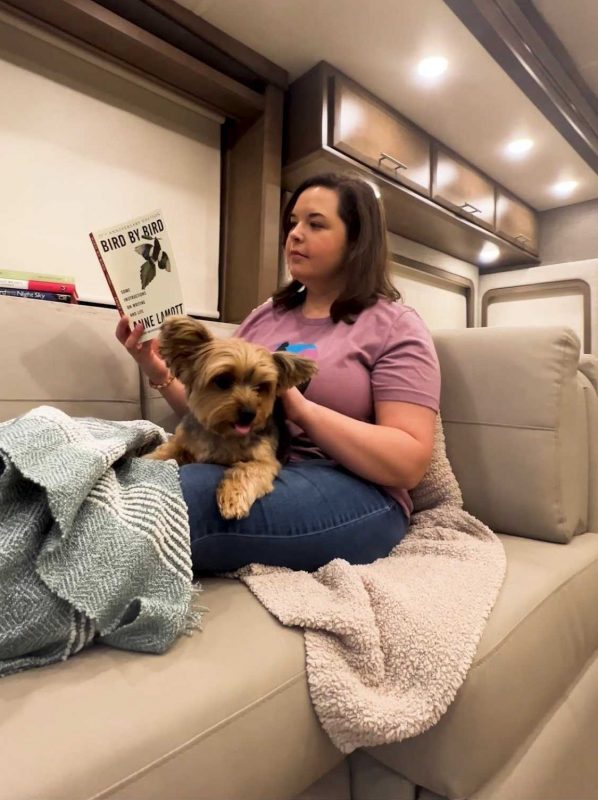 A woman and her dog sitting in an RV relaxing on the couch.